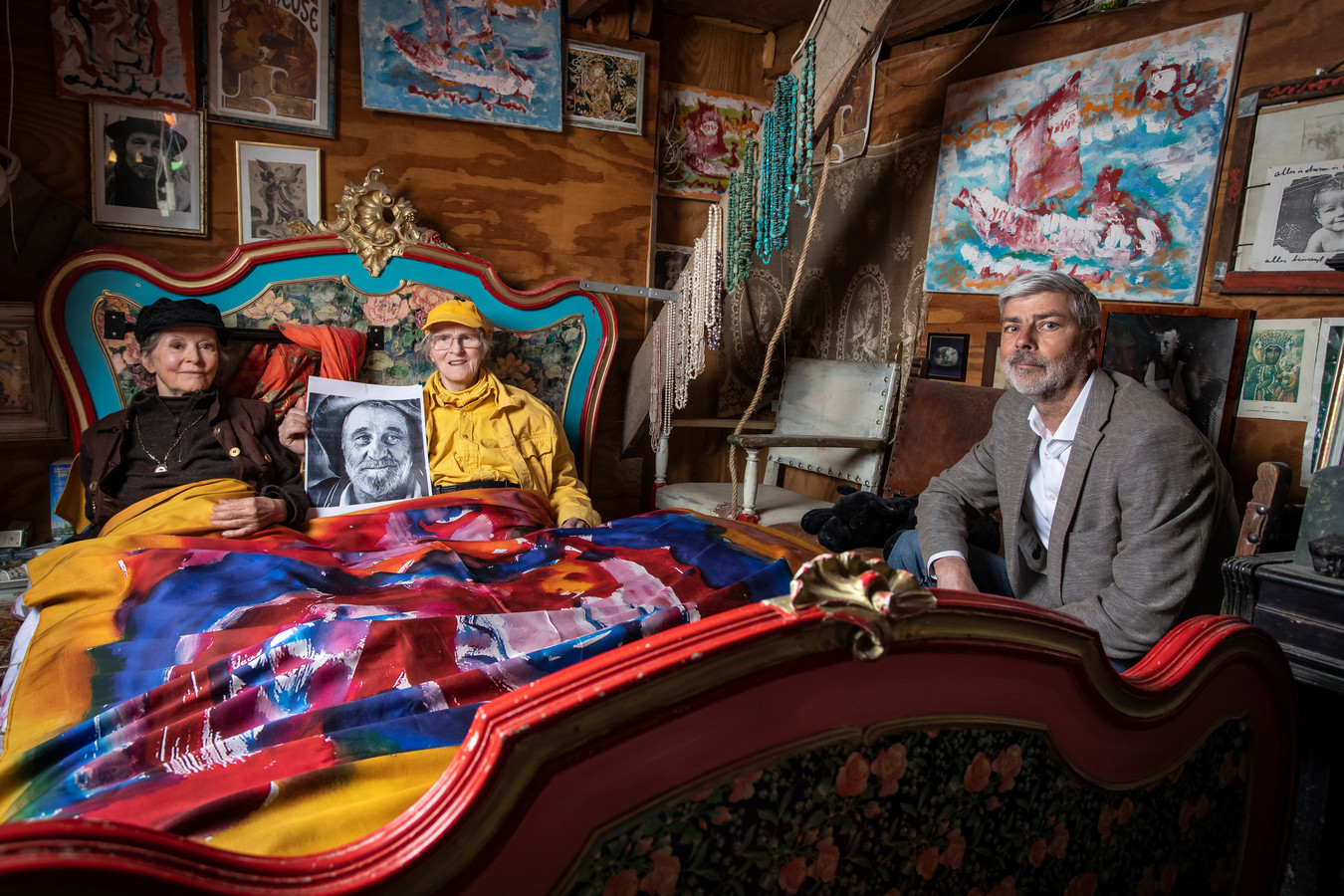 Ewald Poorthuis, directeur Twentse Damast, aan de rand van het bed met Joke (in het geel) en Lotti, twee van de ‘bruiden’ van wijlen Anton Heyboer. Ze liggen onder het dekbedovertrek met afdruk van Hyboers schilderij ‘De Danseres.’