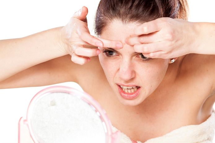 young woman squeeze her acne in front of the mirror