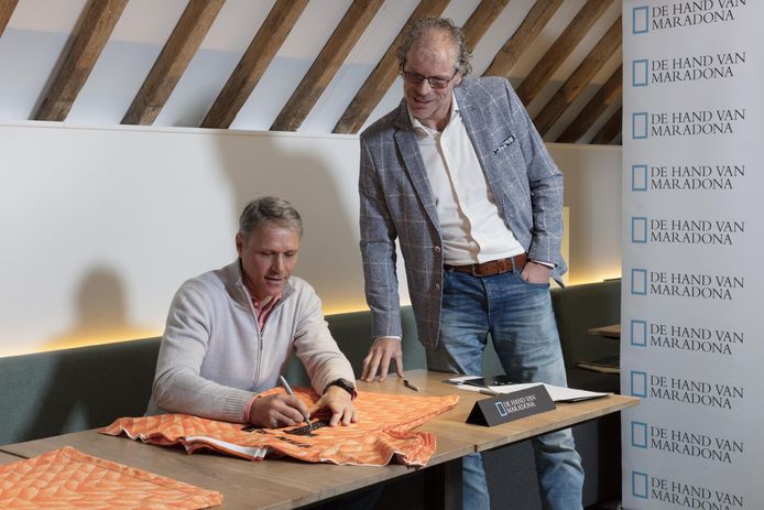 Marco van Basten signeert de shirts met schubmotief, Frank Krake kijkt over zijn schouder mee.
