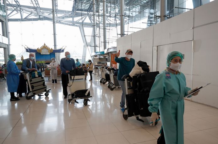Des voyageurs étrangers sont escortés par des employés d'hôtel en combinaison de protection après leur arrivée le premier jour de la réouverture du pays aux visiteurs étrangers à l'aéroport international Suvarnabhumi de Samut Prakan, en Thaïlande, le 1er novembre 2021.