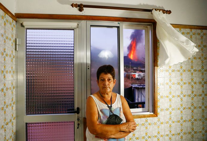 Maria Jesus voor het raam in haar huis in El Paso op La Palma. Op de achtergrond spuwt de vulkaan volop lava en assen uit. Beeld van 4 oktober.