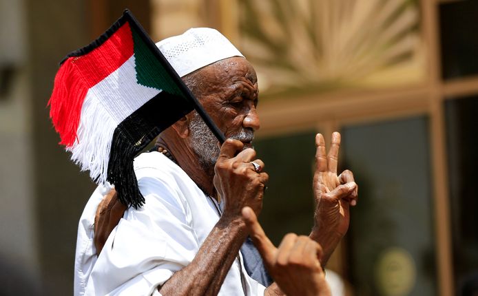 Een man draagt een Sudanees vlaggetje en maakt het vredesteken.
