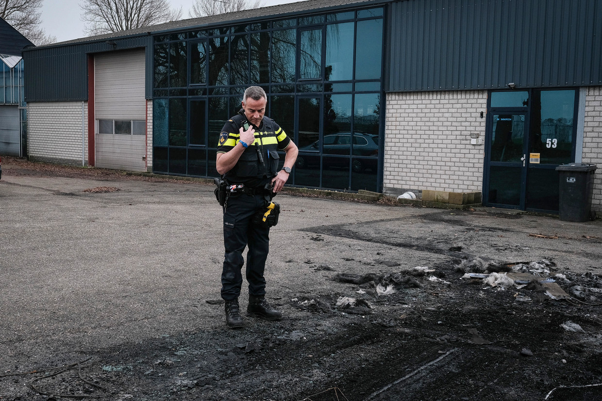 Een politieagent bekijkt de resten van de auto die in de buurt van het huis van de Westlandse kweker Paul Fransen in brand is gestoken. Beeld Daniel Rosenthal / de Volkskrant