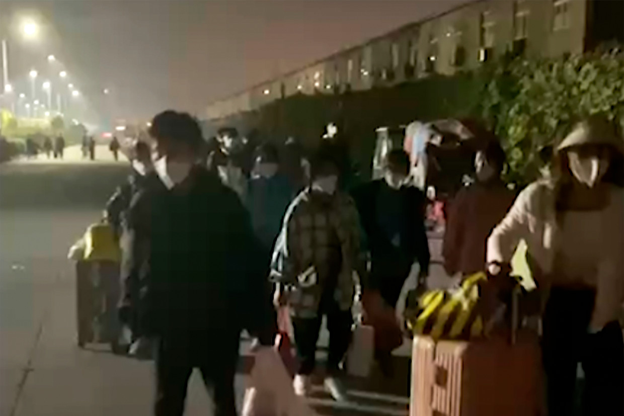 Mensen met koffers en zakken verlaten de Foxconn-fabriek in Zhengzhou. Beeld AP