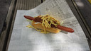Chili Chief Dog (Daily Dog): Pikante hotdog met chilisaus op frisse ijsbergsla met krokante topping.