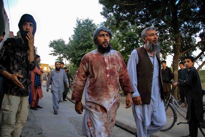 Mensen lopen met bebloede kleding weg van de plaats van een bomaanslag op een moskee in Kaboel.
