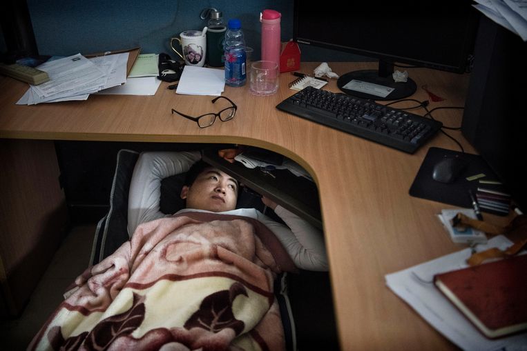 Een werknemer van Huawei kijkt tv op zijn smartphone terwijl hij, zoals vele Chinezen, onder zijn bureau rust tijdens zijn lunchpauze. Beeld Getty Images