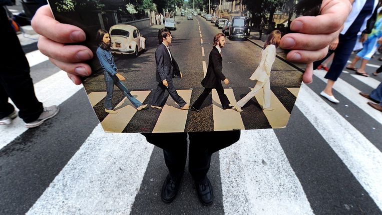 Een tourgids met een albumcover van Abbey Road, op het beroemde zebrapad in Londen. Beeld epa