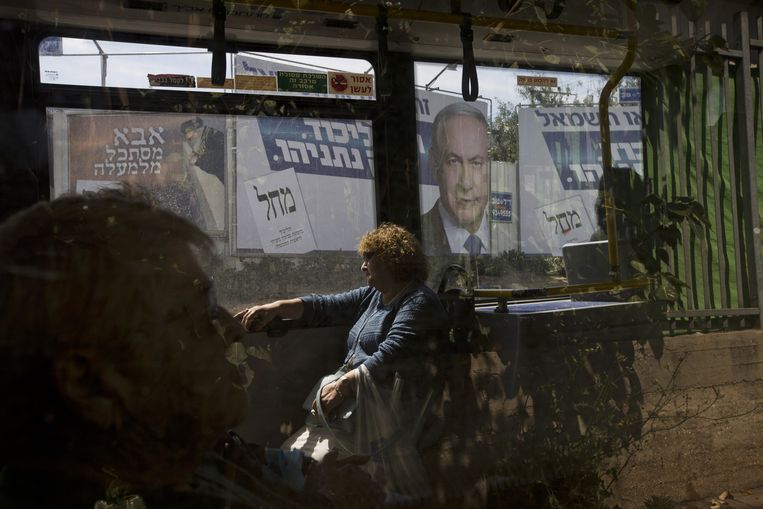 Een passagier zit in een bus die langs een een verkiezingsposter van Netanyahu rijdt. Beeld ap