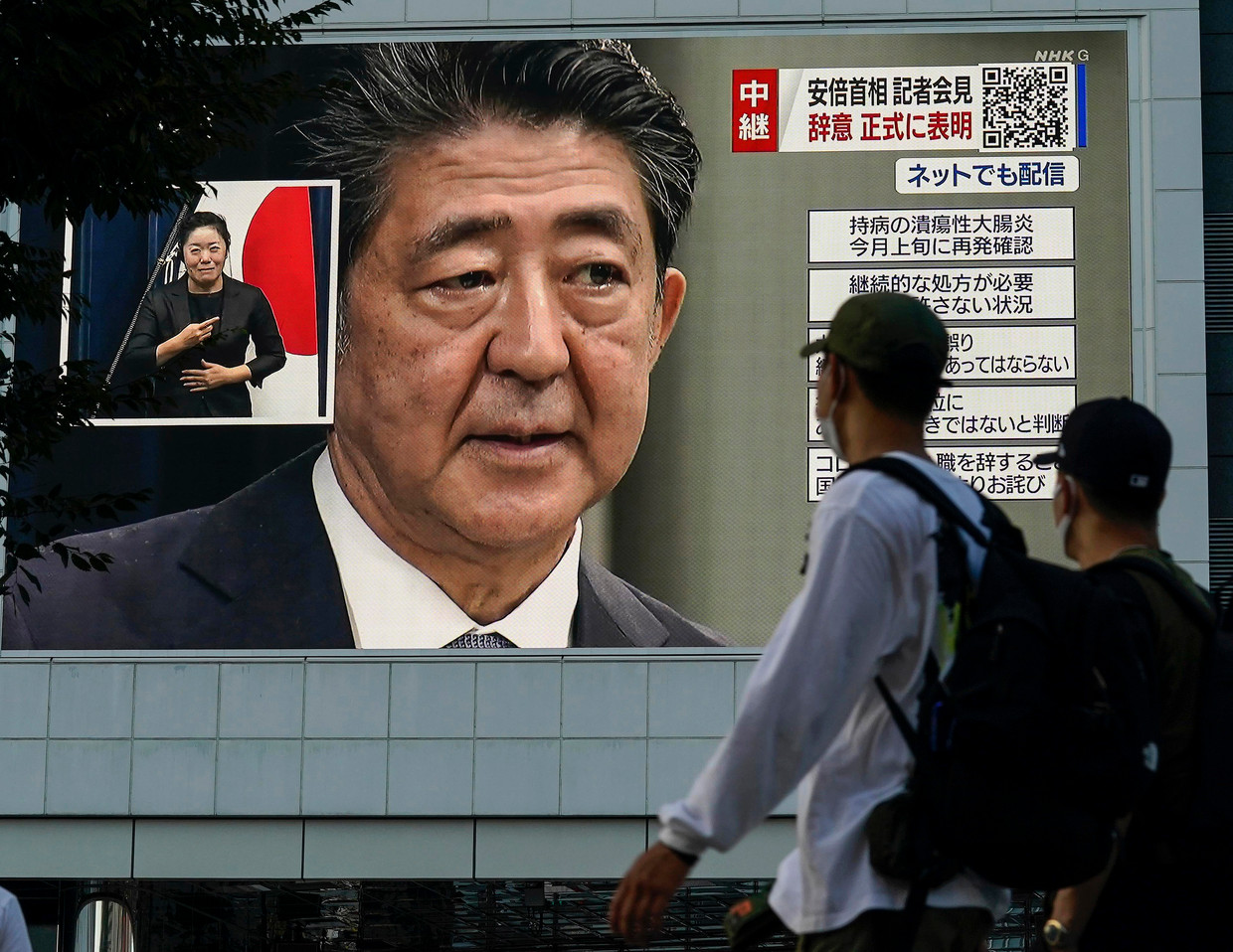 Voorbijgangers in Tokio passeren een enorm tv-scherm waarop premier Abe zijn vertrek bekendmaakt.  Beeld EPA