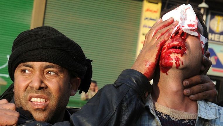 Een Egyptische man helpt een gewonde anti-Mubarakdemonstrant in Caïro. Beeld afp