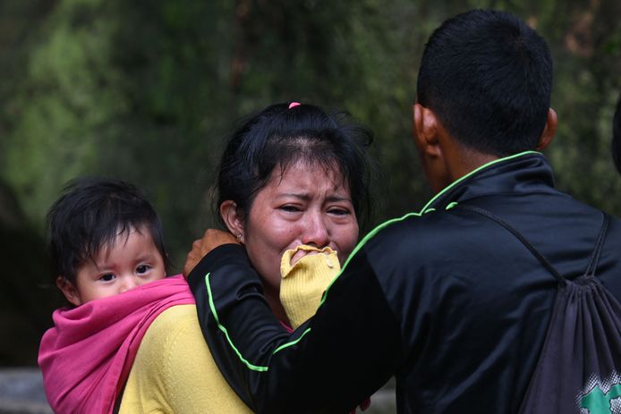 Een vrouw met een baby op haar rug huilt op de plek waar de rivier meerdere huizen meesleurde in een sloppenwijk in Guatemala-Stad.
