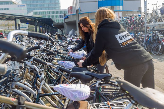 Lotte Heemskerk (l) en Marleen Tempelaars voorzien een paar honderd fietsen op het station van een zadelhoesje.