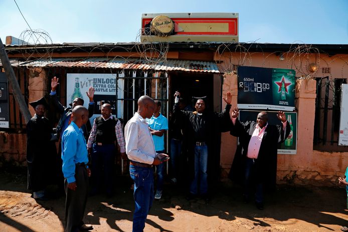 Kerkgangers worden verwelkomd bij de ingang van een bar in Orange Farm, ten zuiden van Johannesburg.