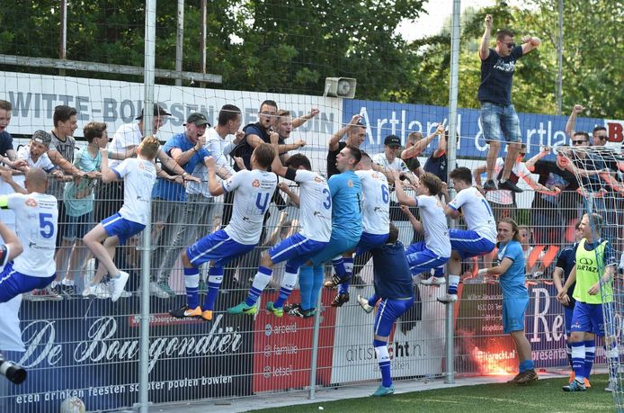 De spelers van Hoek klimmen in de hekken en vieren de promotie met de aanhang.