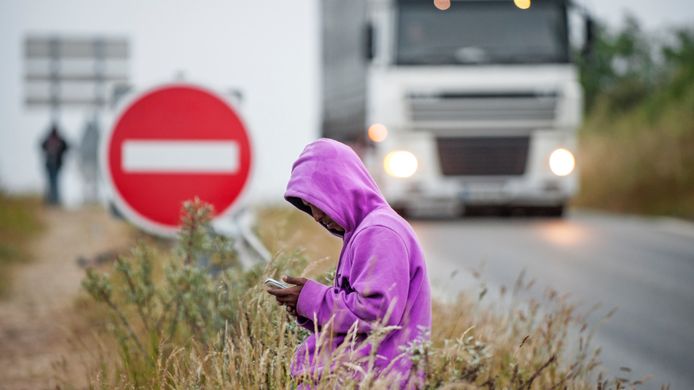 Een vluchteling zit op de vangrail bij een oprit langs de snelweg naar de veerhaven van Calais.  Veel vluchtelingen willen via Frankrijk Engeland bereiken.