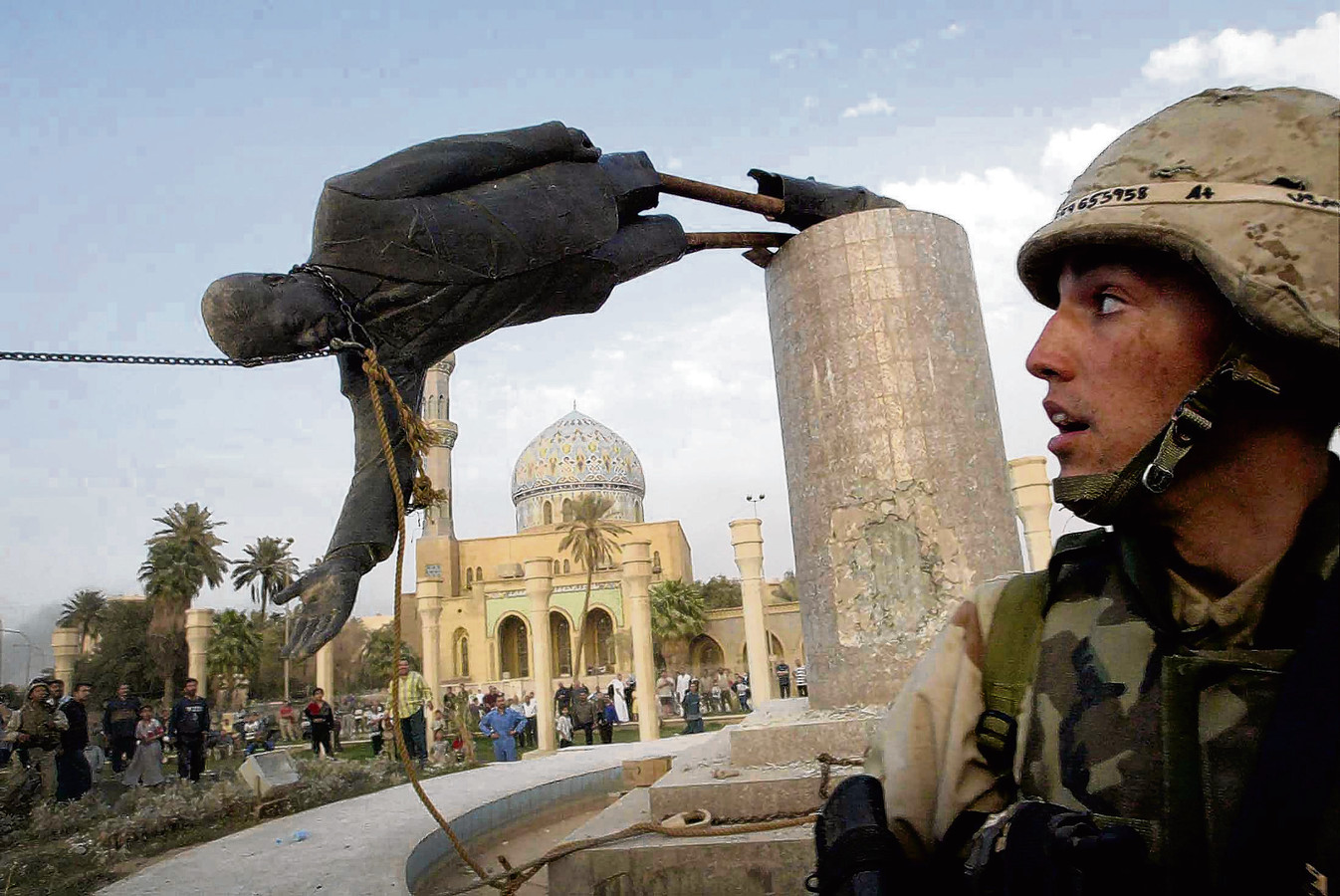Een Amerikaanse militair kijkt op 9 april 2003 toe hoe het standbeeld van Saddam Hussein van zijn sokkel wordt getrokken in het centrum van Bagdad.