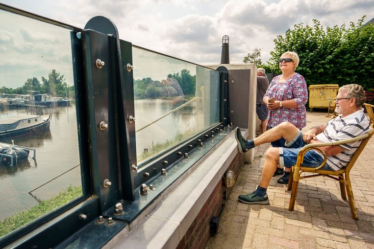 Vrijwilligers van Watersportvereninging Wansum in Neer, Jacqueline Korsten en Max Touw (stoel) zitten tevreden achter de glazen waterkering die er pas sinds februari staat. Beeld Maikel Samuels