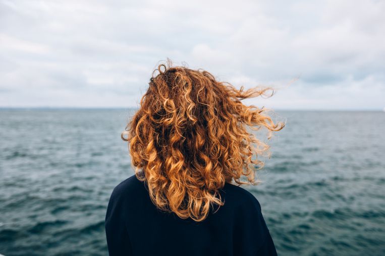 View from the back of a woman with curly hair looks at sea Beeld Getty Images / iStockphoto