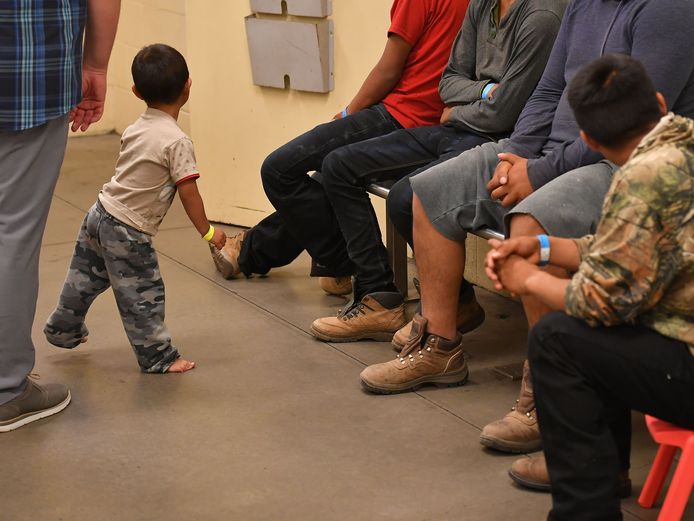 Jongen migrantenkinderen en hun ouders wachten in een detentiecentrum.