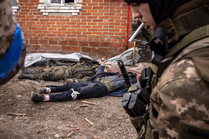 Een Oekraïense militair nabij de lichamen van twee dode Russische militairen in Charkiv.