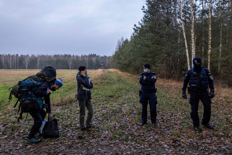 Twee hulpverleners (links) stuiten aan de Poolse kant van de grens met Wit-Rusland op  politieagenten.  Beeld AFP