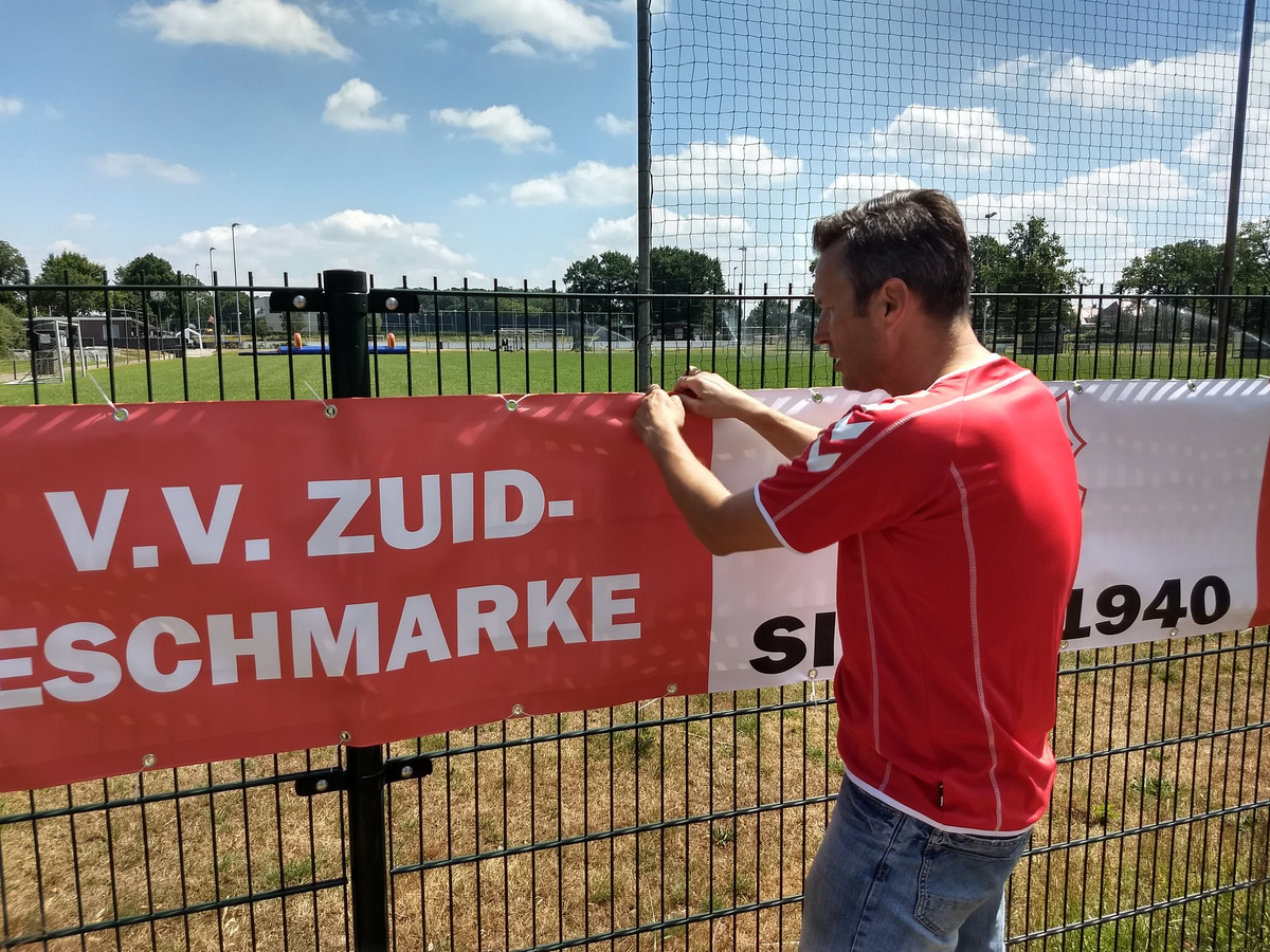 Voorzitter Bas Veenendaal bevestigt het spandoek van Zuid Eschmarke aan het hek van Sportclub Enschede.