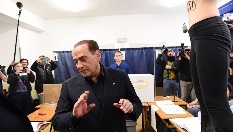 In het stemlokaal waar Silvio Berlusconi zijn stem uitbracht protesteert een halfnaakte jonge vrouw. Op haar buik staat: 'Berlusconi, jouw tijd is voorbij'. Beeld afp