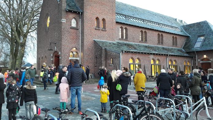 Ouders en kinderen verzamelen zich bij het kerkgebouw voor de eerste schooldag.