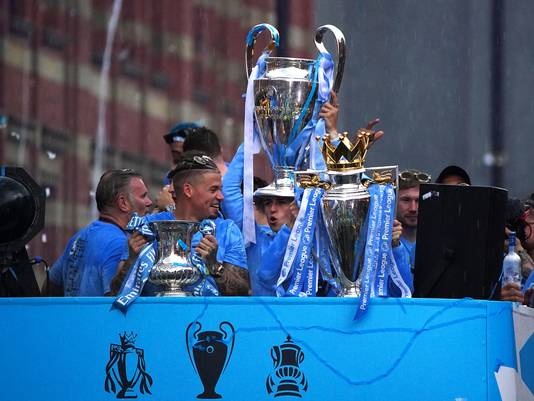 Kalvin Phillips (l) met de FA Cup, Phil Foden heeft de Champions League-cup op z'n hoofd en Bernardo Silva (r, niet zichtbaar) met de trofee van de Premier League. Kevin De Bruyne bekijkt het met feestbril op.