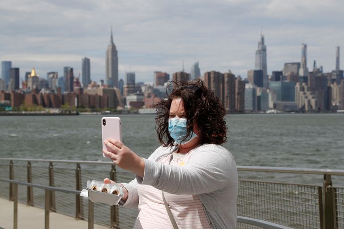 Een vrouw met mondkapje neemt een selfie met de skyline van New York op de achtergrond.