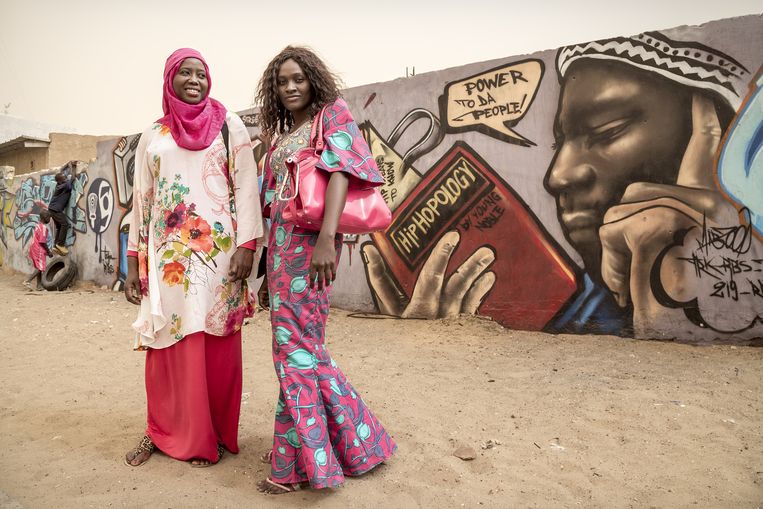 Twee vrouwen, de een met hoofddoek, de ander zonder, op een bushalte in Dakar. Beeld Sven Torfinn / de Volkskrant