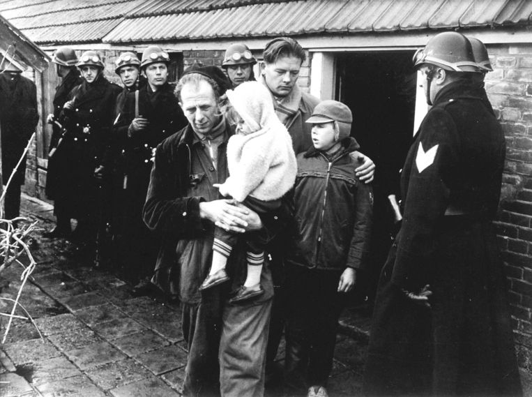 Onder gewapend geleide verlaat ‘vrije boer’ Hartman in 1963 met zijn kinderen de boerderij in Hollandscheveld. Achter hem Evert Harmsen, bestuurslid van de ‘Vrije Boeren’. Beeld Hollandse Hoogte /  ANP