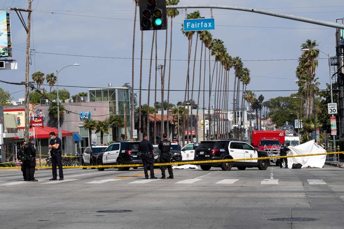 Politie aan de hoek van Fairfax Avenue en Sunset Boulevard. Achter de agenten ligt een lichaam onder een wit laken op de weg, omsloten door politievoertuigen.