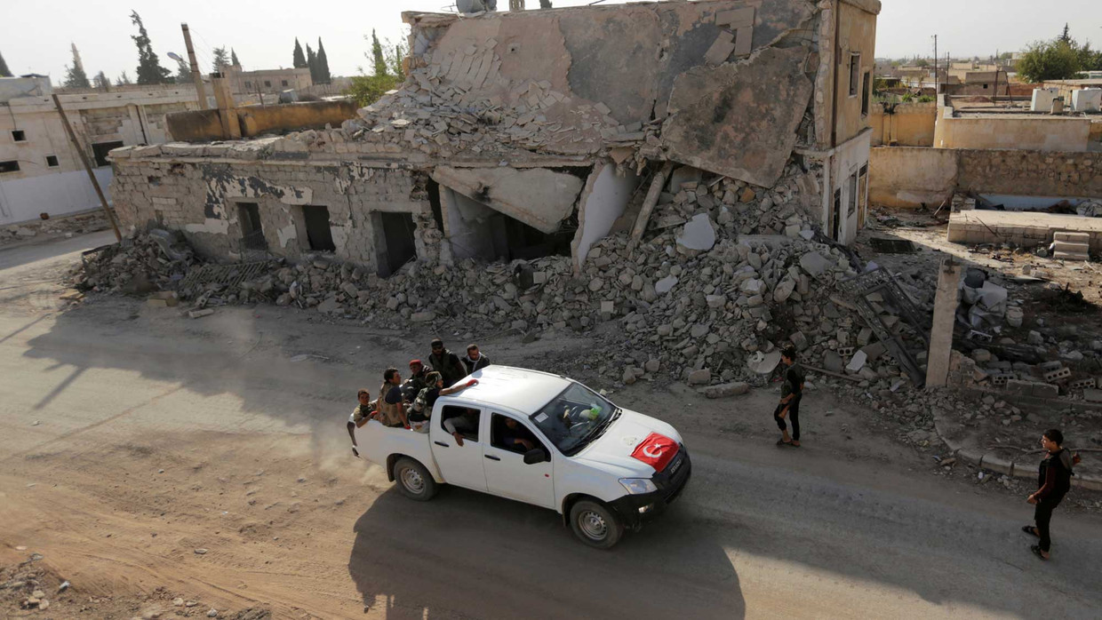 Strijders van het Vrije Syrische Leger in een pick-up truck met een Turkse vlag rijden langs kapotte gebouwen in het noord-Syrische al-Rai, in de regio Aleppo. Beeld Reuters