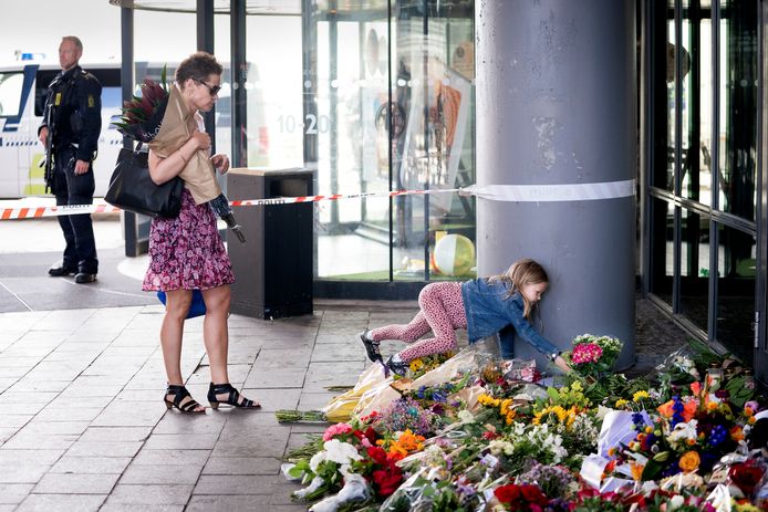 Mensen leggen bloemen neer aan de ingang van het winkelcentrum waar zondag drie mensen werden gedood bij een schietpartij.