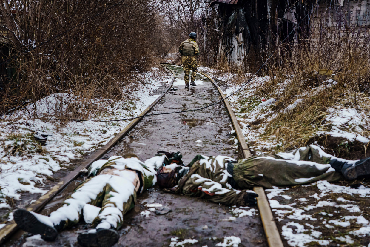 Twee dode Russische soldaten op een spoorlijn bij Irpin, woensdag, met op de achtergrond een Oekraïense soldaat op inspectie. Beeld Los Angeles Times via Getty