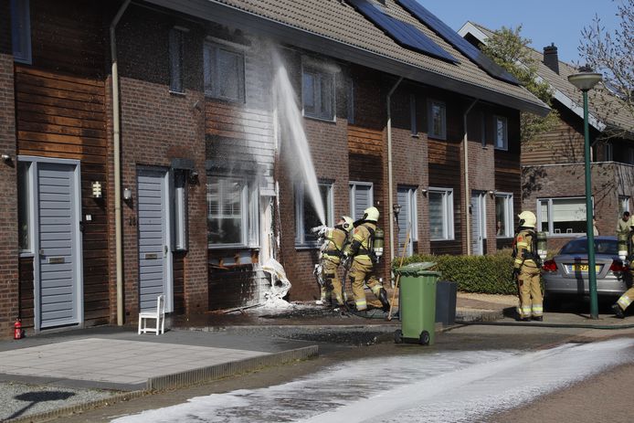 Brandweerlieden blussen houtwerk van een woning aan de Marjolein in Cuijk dat in brand staat.