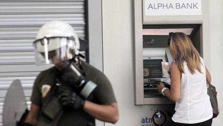 Een vrouw haalt geld uit een pinautomaat terwijl een agent op wacht staat. Beeld epa