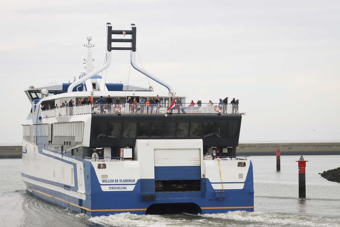 Een veerboot met de Nederlandse vlag half stok vertrekt uit de haven van Harlingen.