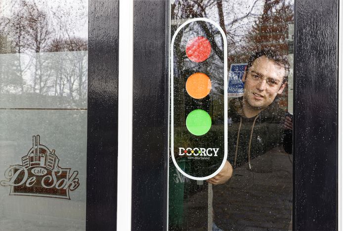 Thomas de Groot plakt een slim stoplicht op de voordeur bij zijn café De Sok in Schijndel.