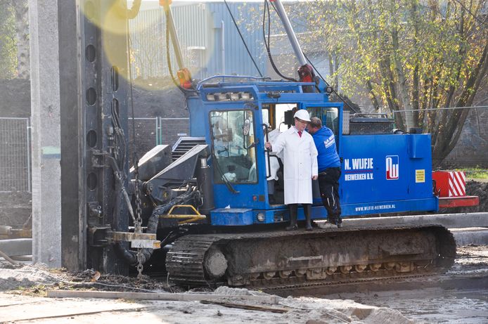 Wethouder Kees van Velzen staat op de rupsband van de kraan die de ‘eerste’ heipaal voor het nieuwe pand van Kaju Putih aan de Dennenlaan de grond in drukt.