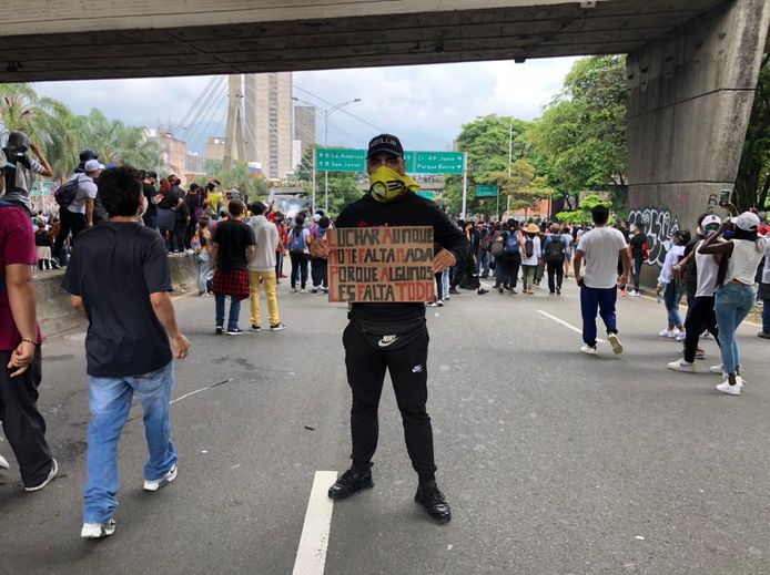 Yino Diaz tijdens het protest in Medellín. Op het bord: 'Ook al kom je zelf niks tekort, vecht voor degenen die alles tekort komen.’