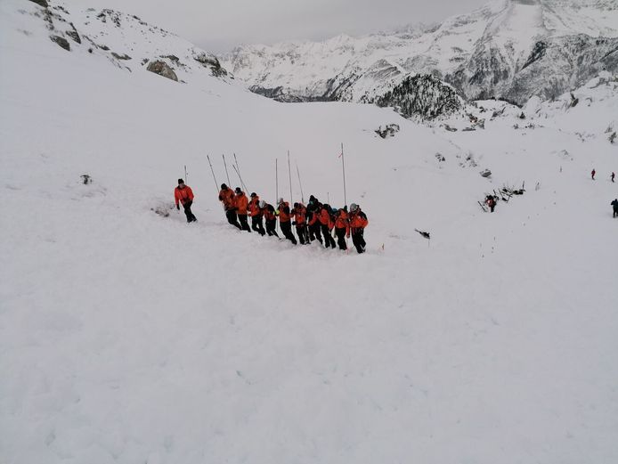 Bergredders tijdens hun zoekactie met prikstokken  naar de onder de sneeuw bedolven skiërs.