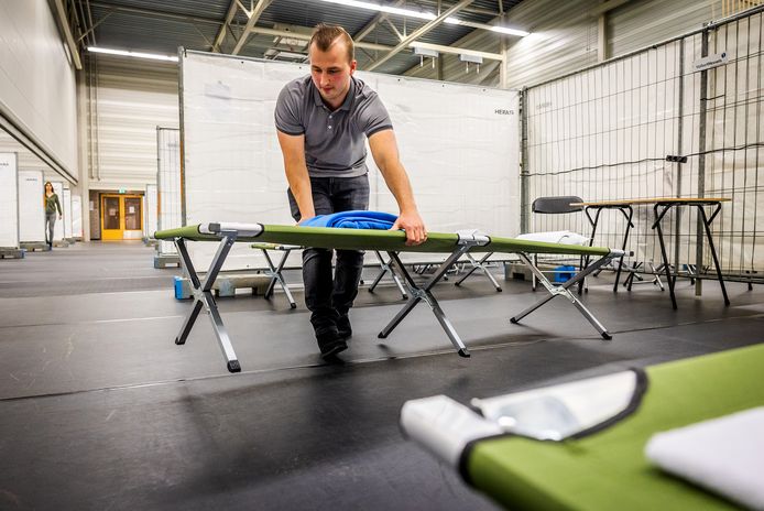 Een medewerker zet een veldbed klaar in sporthal De Hoefslag. Deze noodopvang gaat 7 mei dicht.