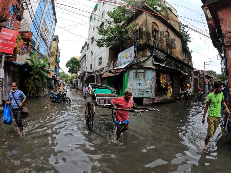 Een riksjarijder trekt eind juli in Kolkata, India zijn kar door straten die overstroomd zijn als gevolg van de hevige moessonregens. Beeld Getty