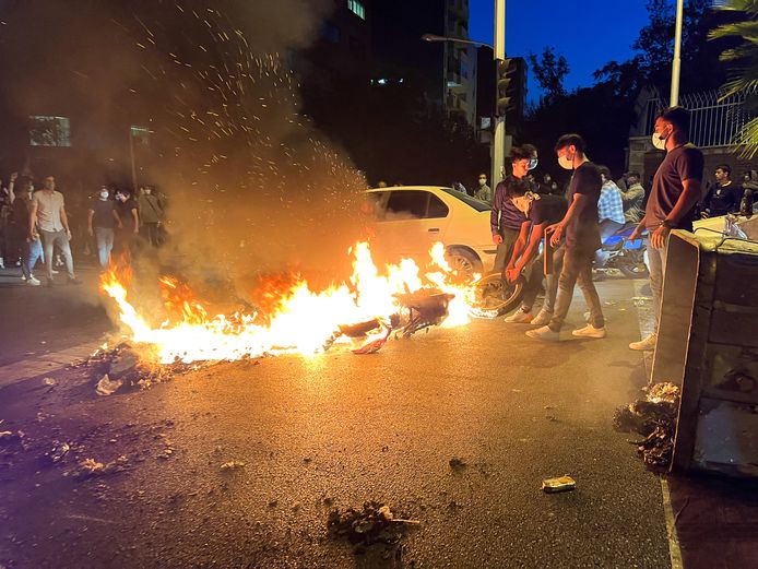 Demonstranten in Iran bij een in brand gestoken politiemotor.
