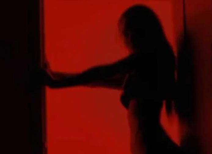 Een vrouw poseert schaars gekleed in een deuropening.