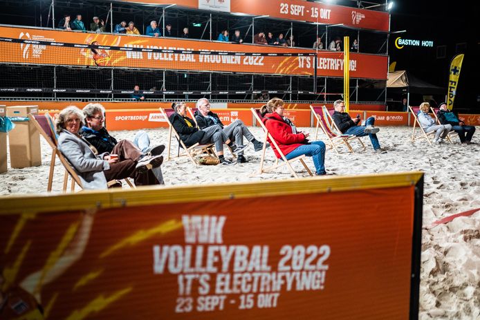 Publiek neemt plaats op de tribune of op een strandstoel in het zand.