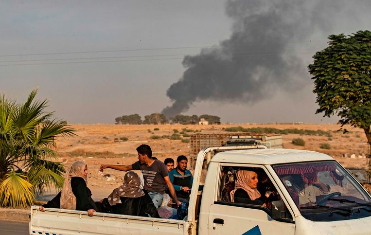 Burgers in een wagen terwijl op de achtergrond de rook opstijgt na een Turks bombardement in de Syrische grensstrook.  Beeld AFP
